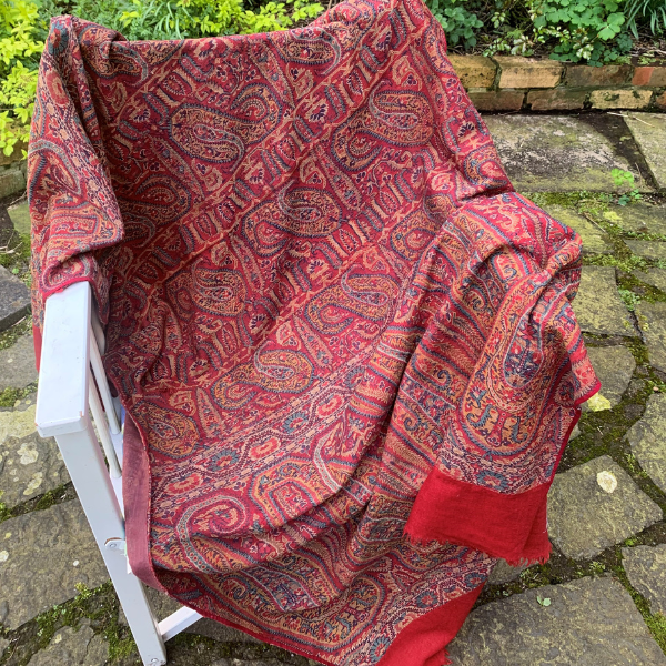 Photo of a red and orange sari with sophisticated pattern and red band around the edges laid on a chair in a garden